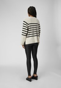 Beige og sort stribet sweater med en afslappet pasform, der har droppe skuldre og en høj-lav kant. Den er sat sammen med skinnende sorte leggings og sko med blokhæle.