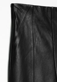 Prenda de cuero negro con una textura suave, que presenta detalles de costura y costuras en ángulo, mostrando un diseño estructurado.