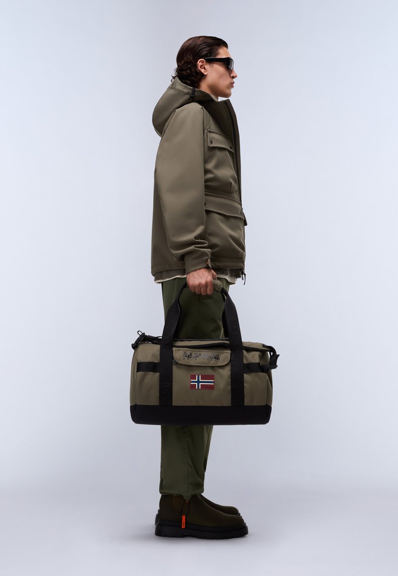 Sac de sport vert olive avec des accents noirs, des poignées et un écusson du drapeau norvégien. Matériau doux, forme cylindrique, avec des détails de fermeture éclair et de boucle.