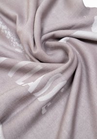 Sciarpa di tessuto grigio chiaro con una texture liscia, caratterizzata da motivi bianchi astratti. Il materiale si drappeggia dolcemente, mostrando morbide pieghe.