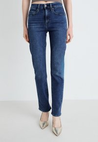 Temno modri jeans z ravnim krojem, visoko pasom, petimi žepi in rahlim zbledelostjo na stegnjih, v kombinaciji z metalnimi čevlji s koničastim nosom.