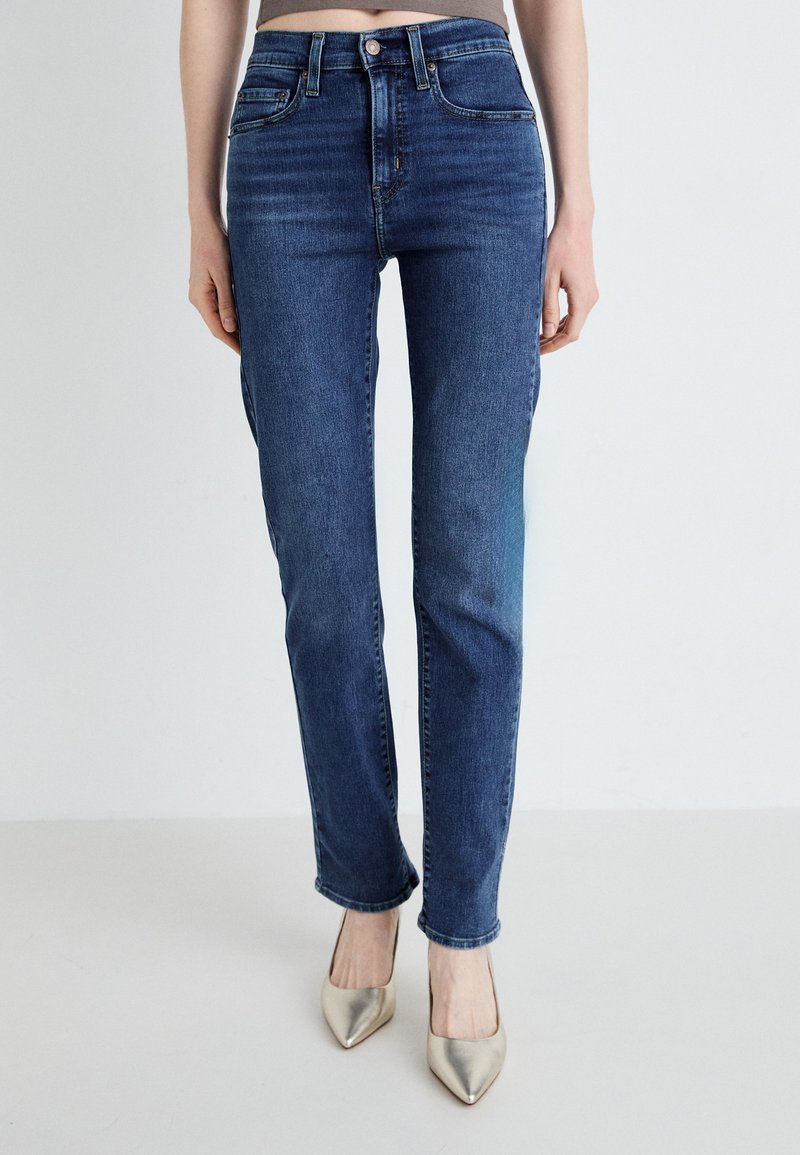 Temno modri jeans z ravnim krojem, visoko pasom, petimi žepi in rahlim zbledelostjo na stegnjih, v kombinaciji z metalnimi čevlji s koničastim nosom.
