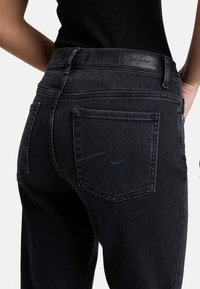 Schwarze Jeans aus Denim mit hohem Bund, zwei Gesäßtaschen und dezenten Nähten. Der Stoff hat ein glattes, strukturiertes Aussehen.