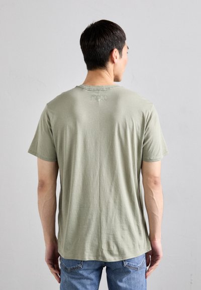 T-shirt vert olive à manches courtes en tissu doux, avec un détail de couture au dos. Le tissu a une texture lisse et une coupe décontractée.