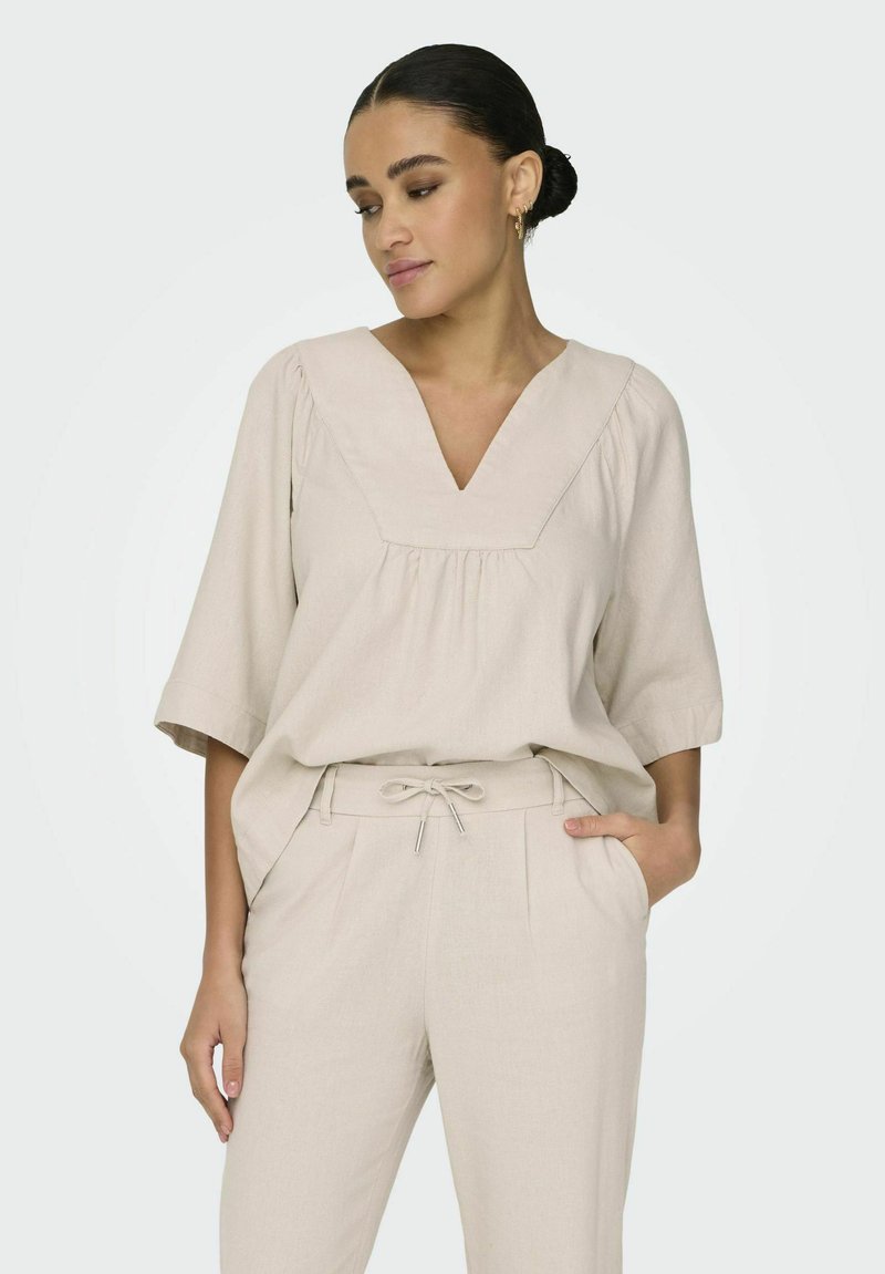 Lichtbeige linnen top met een V-hals en plooien, gecombineerd met bijpassende tapered broek met een verstelbare trekkoord in de taille.