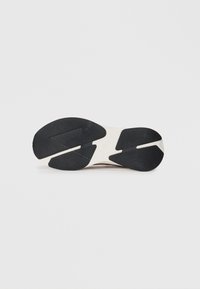 Schuhsohle mit einem strukturierten schwarzen Muster, Details einer hellen Zwischensohle, die ein stromlinienförmiges Design und eine geschwungene Form aufweist.