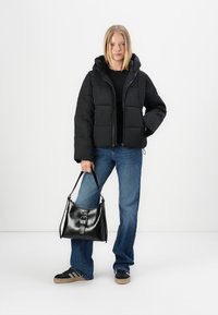 Chaqueta de plumas negra con capucha, diseño acolchado, cierre delantero, combinada con jeans de pierna ancha azules y un bolso negro de hombro con hebilla.