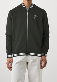 Černá bomber bunda s bílými pruhovanými žebrovanými manžetami a límcem, zapínání na zip vpředu a vyšívaným logem na hrudi.