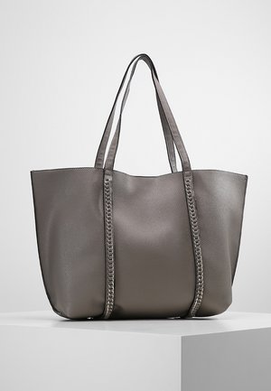 Szara torebka typu tote z teksturowanej skóry z dwoma długimi uchwytami i pionowymi przeszyciami, stojąca na białym piedestale.