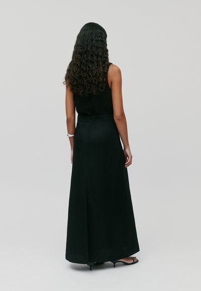 Robe maxi noire avec un corsage ajusté et une jupe fluide. Présente une fente discrète à l'arrière et une texture de tissu lisse.