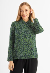 Camicia verde con un motivo a onda in verde scuro e dettagli bianchi, dotata di colletto e maniche lunghe, realizzata in tessuto leggero.