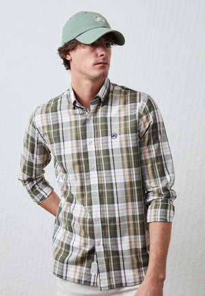 Camisa de cuadros verde, blanca y amarilla con botones, de manga larga, con los puños recogidos y un logo azul en el pecho. Tela ligera.