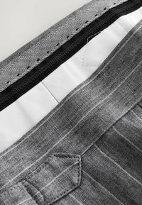 Tissu gris avec des rayures verticales, doté d'une taille en motif chevron et d'un petit détail de poche. L'intérieur est doublé en blanc.