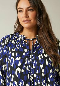 Camicia nera con macchie leopardate blu e bianche, realizzata in tessuto leggero e testurizzato, con scollatura arricciata e dettagli con fiocco nella parte frontale.