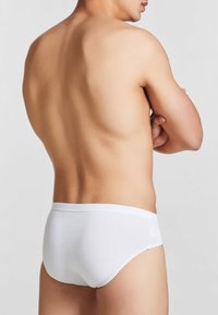 Slip di cotone bianco su un torso maschile nudo, con una texture liscia e un design semplice. L'elastico è senza cuciture.
