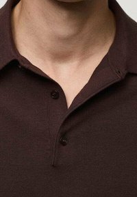Brązowa koszulka polo z dwoma czarnymi guzikami, wykonana z fakturowanej tkaniny. Posiada kołnierzyk oraz krótką plisę przy dekolcie.