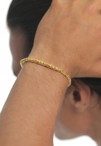 Bracelet en or au design tressé, reposant sur un poignet à peau claire, présentant des détails complexes et une texture lisse.