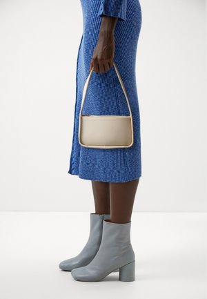 Persona con indosso un vestito blu a costine, stivaletti grigio chiaro alla caviglia e una piccola borsa beige con cerniera superiore e tracolla singola.