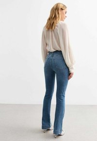 Hoge taille blauwe denim flared jeans met achterzakken en een aangesloten silhouette, gecombineerd met een licht, vloeiend blouse.