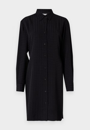 Robe chemise noire à boutons, à manches longues, en tissu texturé et à coupe droite, atteignant la mi-cuisse.