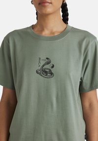 Green cotton t-shirt featuring a black snake graphic and the text "RVCA" with coordinates, in a relaxed fit with a crew neckline.