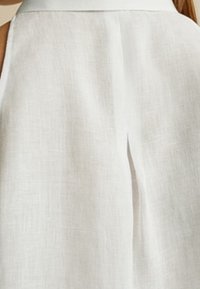 Vestito bianco in lino con un collo alto, linee pulite, spacco posteriore e design minimalista. Texture morbida con un sottile motivo di intreccio.