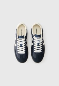 Un paio di sneakers in pelle blu navy e bianche con lacci bianchi, strisce laterali bianche e soletta con marchio su sfondo bianco.