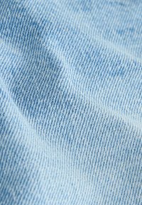 Nærbillede af lyseblåt denimstof, der viser diagonalt vævemønster og subtile skygger på den teksturerede overflade.