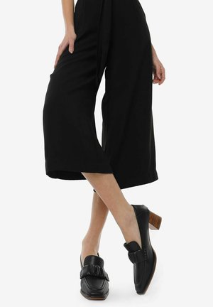 Black leather shoes with a rounded toe and a ruffled accent. They feature a low block heel and a smooth finish.