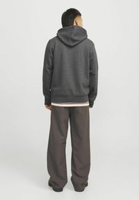 Sudadera gris con capucha ajustable vista desde la parte de atrás, combinada con pantalones de pierna ancha de color marrón oscuro. Material de mezcla de algodón, corte relajado.