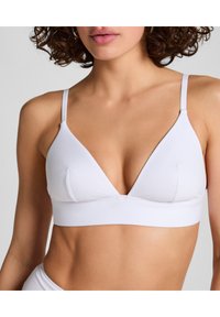 Bralette de algodón blanco con forma triangular, tirantes finos ajustables y una banda de soporte. Textura suave con detalles mínimos.