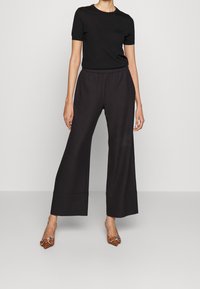 Camiseta negra de manga corta combinada con pantalones anchos negros. Tejido suave con cintura elástica. Zapatos marrones de punta con detalles ornamentales.