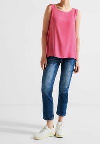 Rosa ärmlös topp i ett mjukt tyg, i kombination med blå denimjeans och vita sneakers. Toppens design har en rund halsringning och en avslappnad passform.