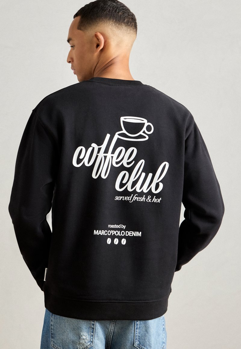Schwarzer Pullover mit weißem Drucktext auf der Rückseite: "Coffee Club frisch und heiß serviert" mit einer Tassen-Grafik und Branding darunter.