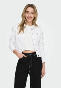 White denim jacket with snap buttons, featuring front pockets and a cropped design, paired with high-waisted black pants with contrasting stitching.