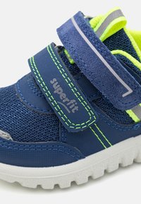 Mørkeblå sneaker laget av mesh og syntetisk materiale, med sterke grønne detaljer, justerbar borrelåsrem og strukturert gummisåle.