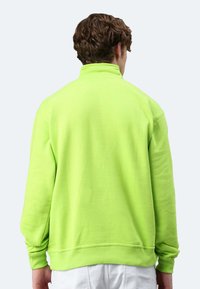 Neon-grüner Sweatshirt aus weichem Stoff, mit hohem Kragen und langen Ärmeln. Die Rückseite ist schlicht mit gerippten Bündchen und unterem Saum.