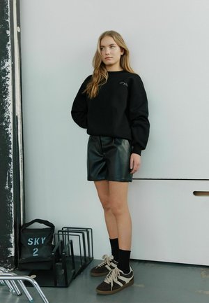 Črna trenirka z rebrastimi manšeti in majhnim logotipom; črne hlače iz umetne usnje; rjavi in beli športni copati; črne nogavice.