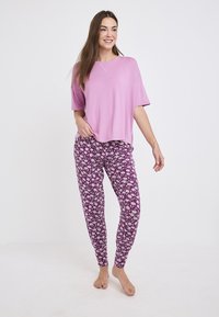 Camiseta rosa de corte holgado con mangas cortas, combinada con pantalones morados ajustados que tienen un patrón floral blanco. Tejido ligero, diseño casual.