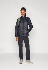 Doudoune bleu marine, avec un col haut et une fermeture éclair. Pantalons noirs avec des poches zippées, associés à des baskets gris clair avec des accents violets.