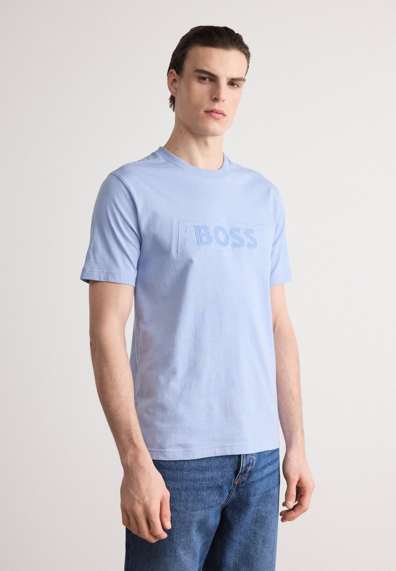 Hele sinine puuvillane T-särk lühikeste varrukatega, mille esipinnal on embosseeritud 'BOSS' logo ja ümmargune kaelus. Seljas sinised denim teksad.