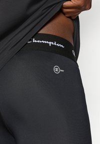 Zwarte sport shorts met het Champion logo op de tailleband en een "DRY" label. Het materiaal lijkt glad en lichtgewicht, ontworpen voor comfort en ademend vermogen.