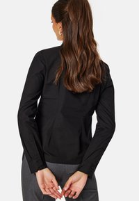 Camicia nera su misura con maniche lunghe, polsini con bottone e design aderente. Tessuto liscio con una leggera lucentezza e linee pulite ed eleganti.