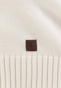 Crème kleurige gebreide trui met ribbelstructuur, voorzien van een vierkant bruine leren label met "KEY LARGO" in zwart geperst.