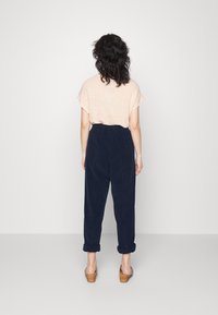 Heledbež žaketiga lühikeste varrukatega topp, mis on kombineeritud tumeda navy sinise kõrge talje pooleliha pükste ja kergete ääretega, millel on elastne vöökoht.