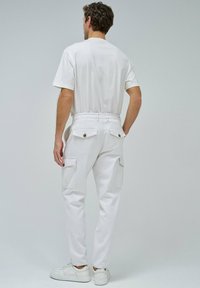 Pantalones cargo blancos con dos bolsillos laterales, un cierre de botón y un diseño de pierna ajustada. Combinados con una camiseta blanca simple y zapatillas blancas.