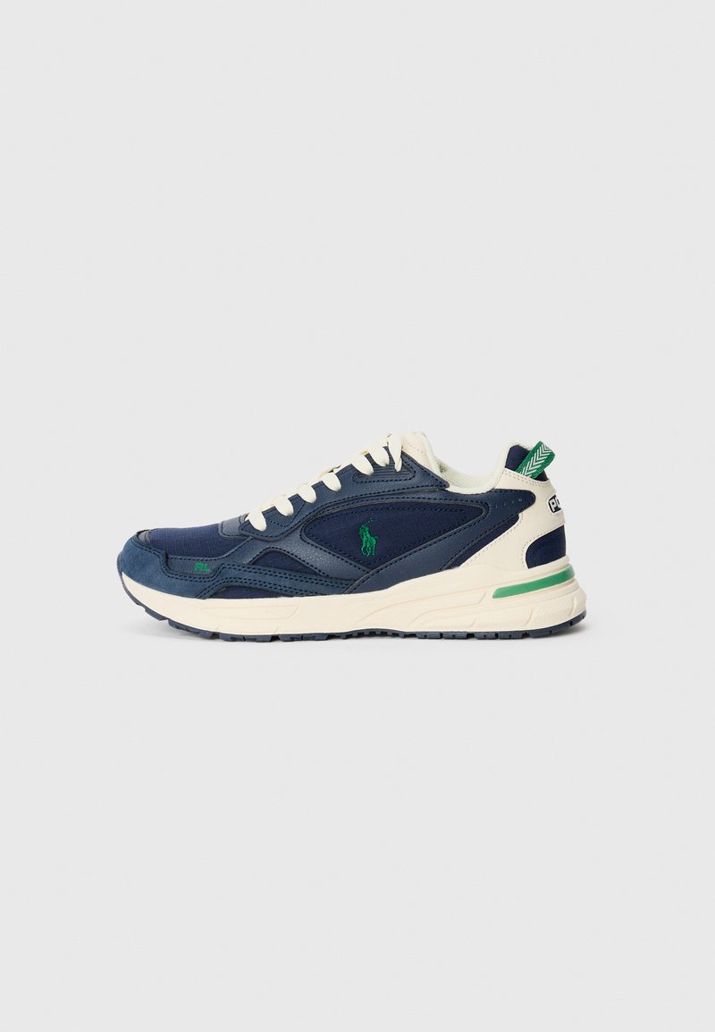 Sapatilha desportiva navy com detalhes em creme, painéis texturizados e logótipo verde. Apresenta um bico arredondado e um design de sola em camadas para suporte.