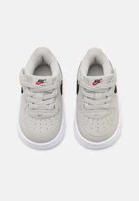 Szürke Nike sportcipők sima felsőrésszel, fekete részletekkel és fehér gumitalppal. Jellemzői közé tartoznak a fűzők, a perforált dizájn és a logó.