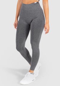 Hoge taille, grijze leggings gemaakt van rekbaar materiaal, met een gladde structuur en geen zichtbare patronen; gedragen met witte sportschoenen.