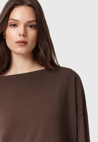 Maglione marrone oversize con un ampio scollo e maniche lunghe e larghe, realizzato in tessuto morbido e liscio. Colore semplice e uniforme con dettagli di design minimi.